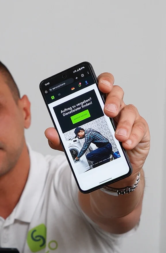Service provider in a white polo holding a phone showing the milles home screen.